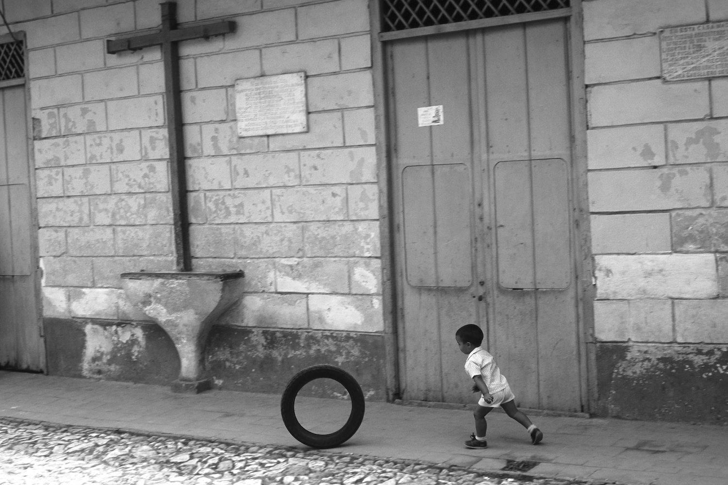 Enfant au cerceau passant près d’un calvaire à Cuba
